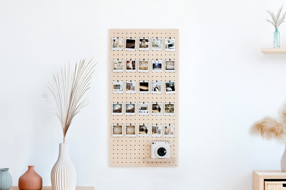 Pegboard en bois fixé au mur d'un salon, utilisé comme mur photo avec des tirages instantanés