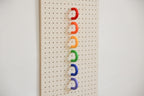 Anneaux colorés rouge, orange, jaune, vert, bleu et violet alignés sur un pegboard en bouleau