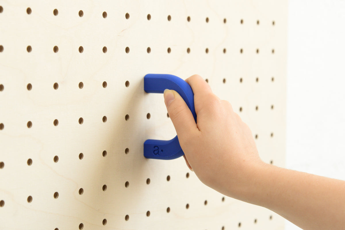 Main fixant un anneau coloré bleu taille M sur un pegboard en bouleau