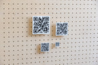 QR codes personnalisés imprimés en 3D en quatre tailles, noir sur blanc, fixés sur un pegboard en bouleau