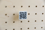 QR code personnalisé 3 × 3 cm imprimé en 3D, noir sur blanc, en gros plan sur un pegboard en bouleau