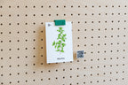 Petit QR code personnalisé imprimé en 3D à côté d'une carte botanique pincée sur un pegboard en bois clair