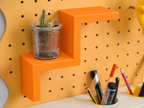 Étagère escalier deux marches orange sur pegboard avec une petite plante