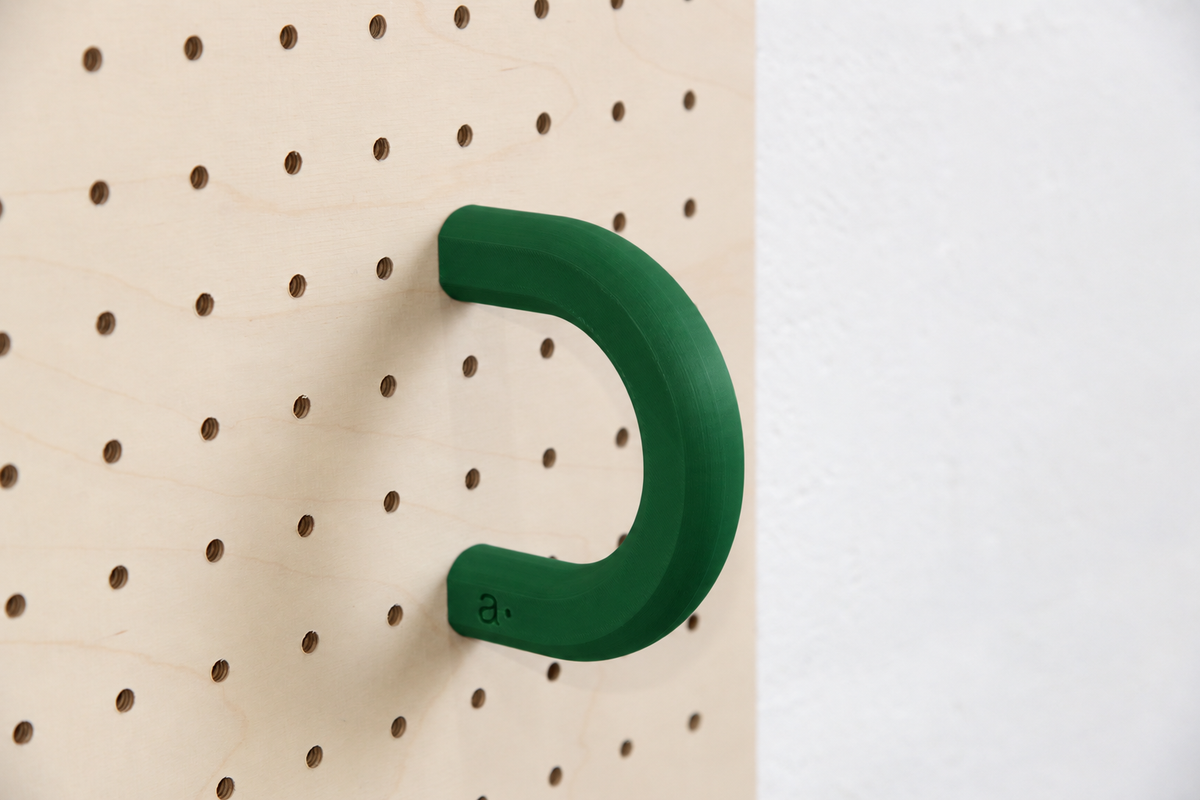 Anilla de color verde oscuro talla L en un pegboard de abedul
