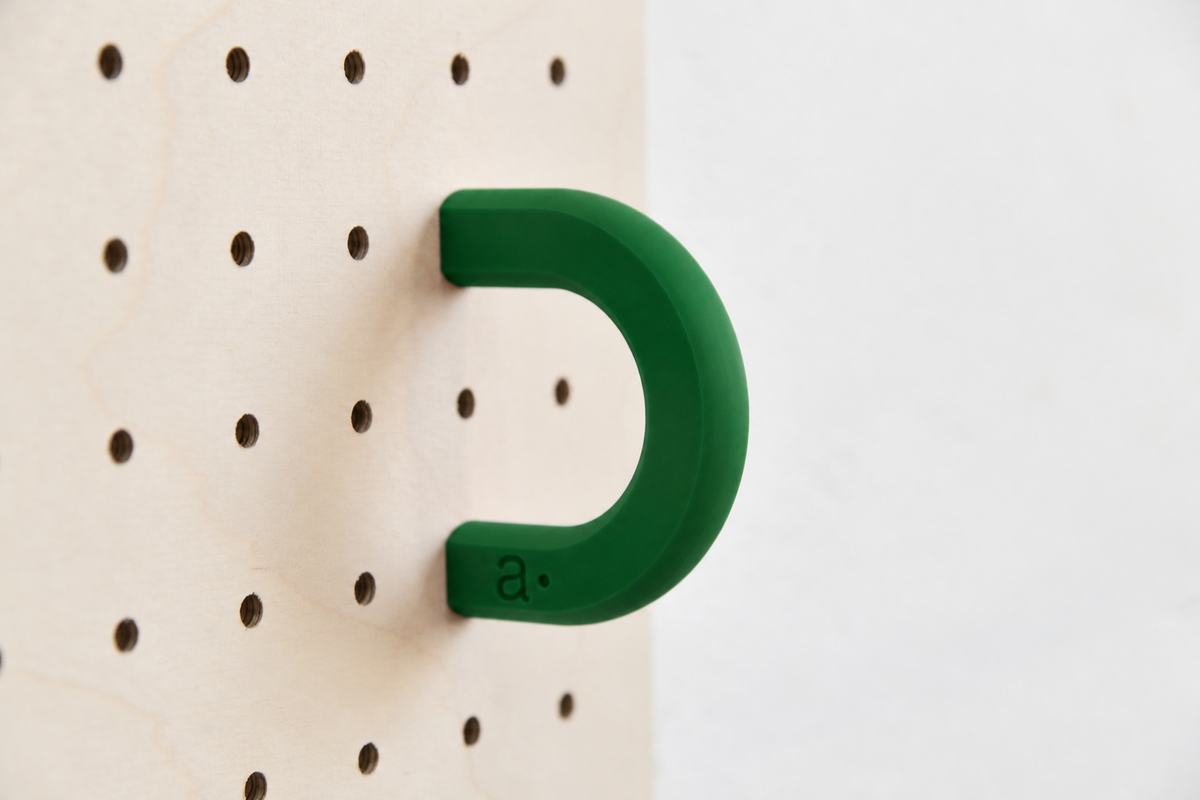 Anilla de color verde oscuro talla M en un pegboard de abedul