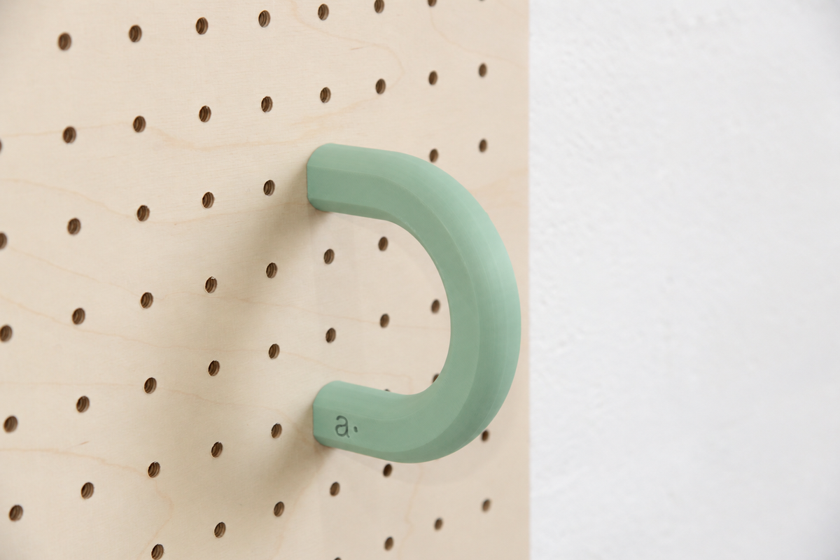 Anilla de color verde salvia talla L en un pegboard de abedul
