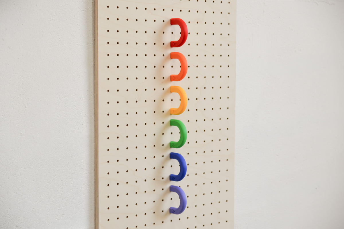Rote, orange, gelbe, grüne, blaue und violette Ringe in einer Reihe an einem Pegboard aus Birke