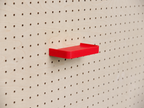 Estante 3D a medida rojo con reborde, montado en un pegboard de madera clara