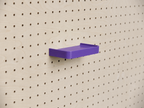 Estante 3D a medida morado con reborde, montado en un pegboard de madera clara