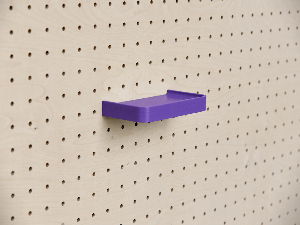Estante 3D a medida morado con reborde, montado en un pegboard de madera clara