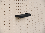 Estante 3D a medida negro con reborde, montado en un pegboard de madera clara