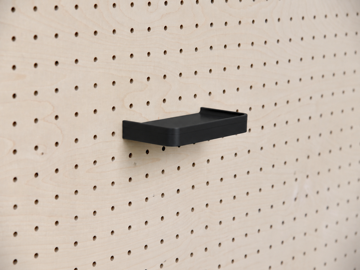 Estante 3D a medida negro con reborde, montado en un pegboard de madera clara