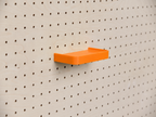 Estante 3D a medida naranja con reborde, montado en un pegboard de madera clara