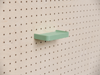 Estante 3D a medida verde salvia con reborde, montado en un pegboard de madera clara