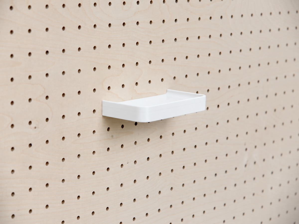 White custom 3D shelf with a raised lip, mounted on a light wood pegboard