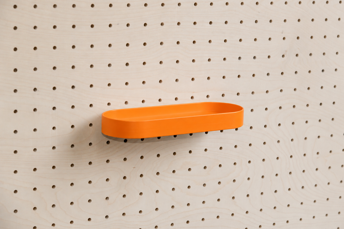 Abgerundetes Regalbrett mit Kanten in Orange an einem Birken-Pegboard, leicht schräge Ansicht mit Schatten