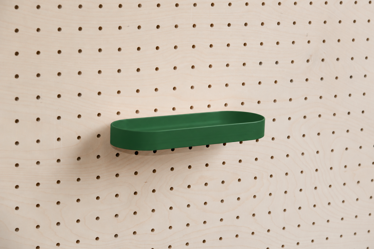 Abgerundetes Regalbrett mit Kanten in Tannengrün an einem Birken-Pegboard, leicht schräge Ansicht mit Schatten