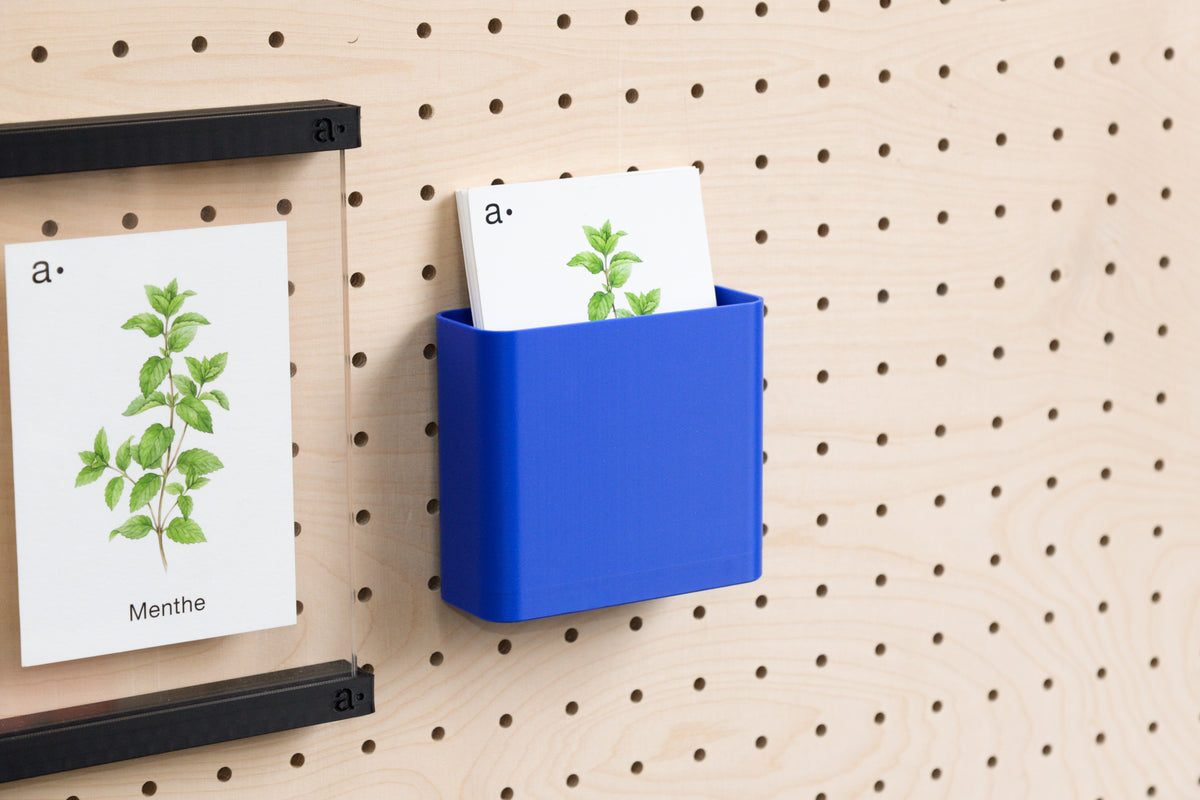 Godet bleu rempli de cartes à côté d'un porte-affiche sur un panneau perforé