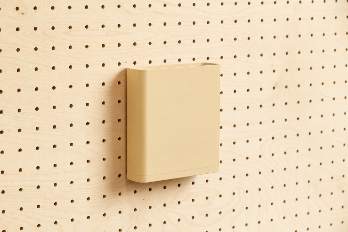 Godet porte-documents beige pour pegboard, seul au centre d'un panneau perforé en bouleau, vue de face