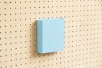 Godet porte-documents bleu ciel pour pegboard, seul au centre d'un panneau perforé en bouleau, vue de face