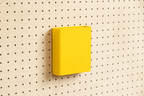 Godet porte-documents jaune pour pegboard, seul au centre d'un panneau perforé en bouleau, vue de face