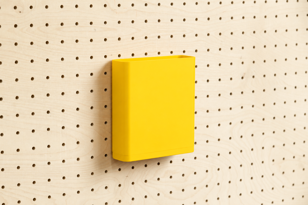 Godet porte-documents jaune pour pegboard, seul au centre d'un panneau perforé en bouleau, vue de face