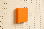 Godet porte-documents orange pour pegboard, seul au centre d'un panneau perforé en bouleau, vue de face