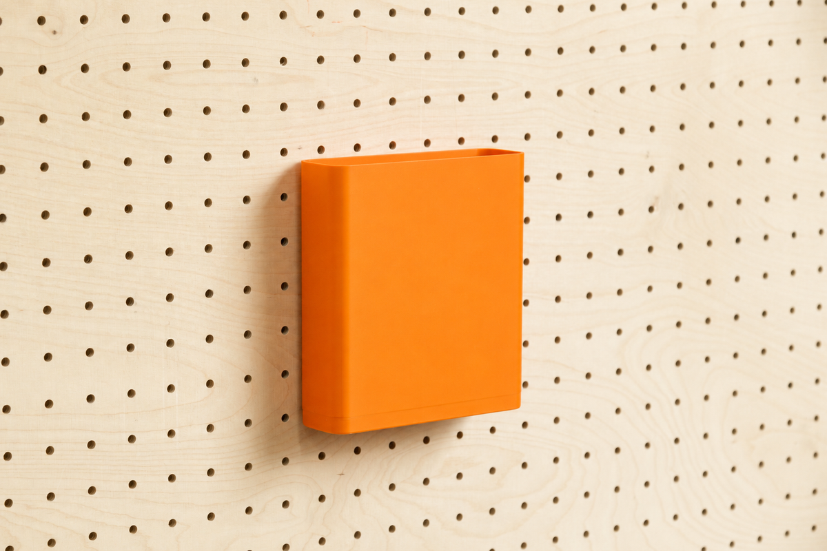 Godet porte-documents orange pour pegboard, seul au centre d'un panneau perforé en bouleau, vue de face