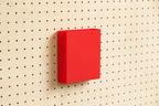 Godet porte-documents rouge pour pegboard, seul au centre d'un panneau perforé en bouleau, vue de face