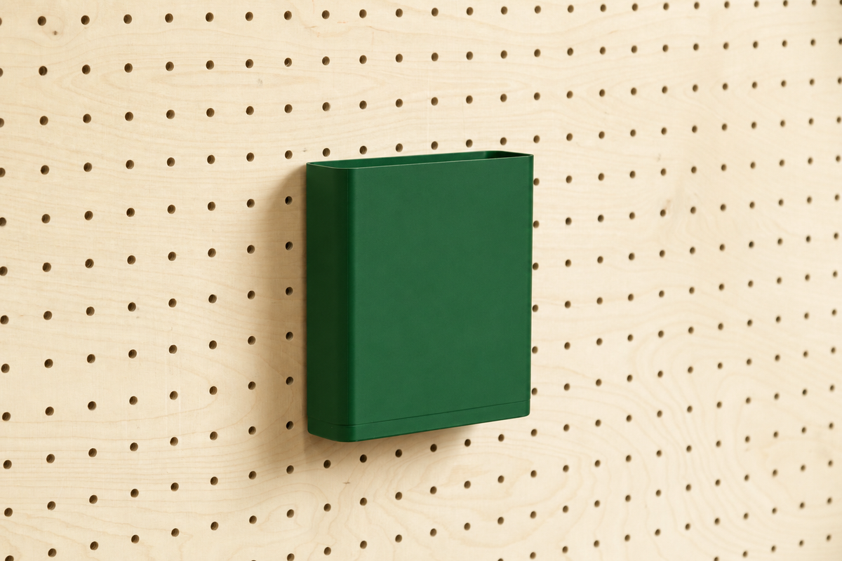 Godet porte-documents vert foncé pour pegboard, seul au centre d'un panneau perforé en bouleau, vue de face