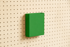 Godet porte-documents vert pour pegboard, seul au centre d'un panneau perforé en bouleau, vue de face