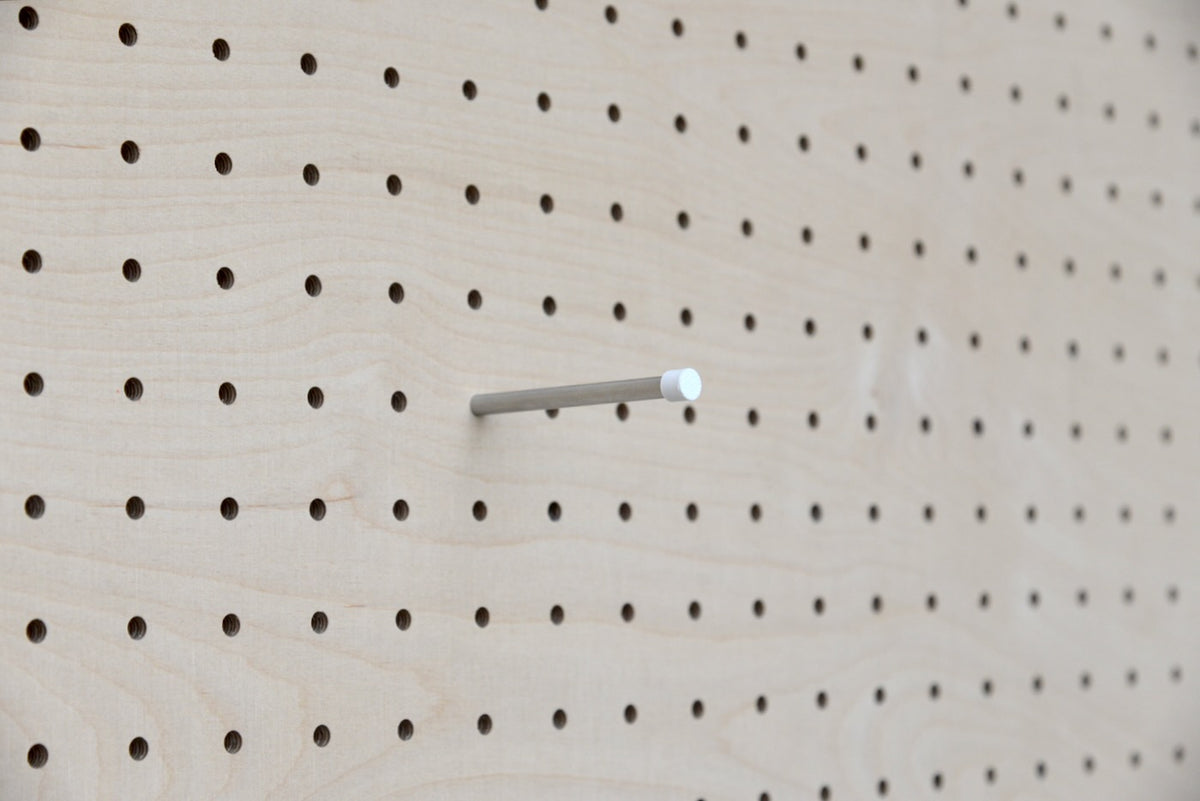 Pasador inox para pegboard con tope de color blanco, clavado en un panel perforado de madera