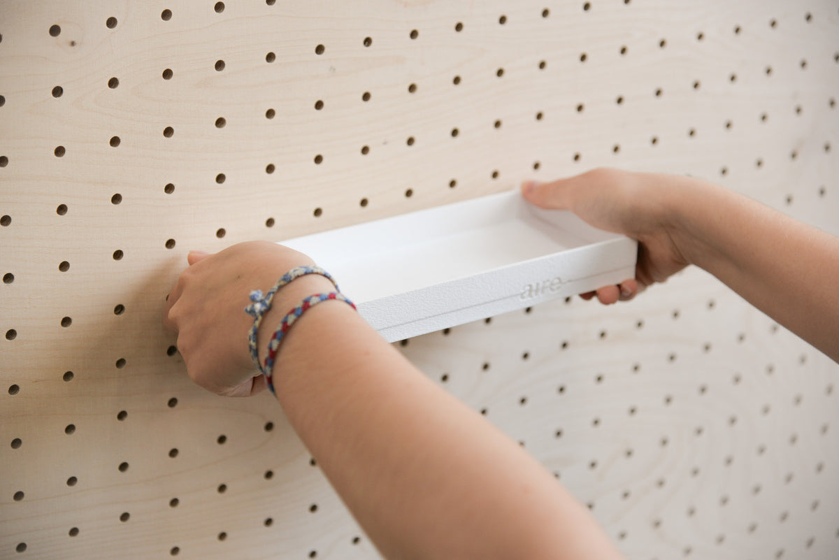 Mains installant une étagère avec rebords blanche sur un pegboard en bouleau