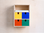 Wand-Organizer aus Birke mit gelber, blauer, roter und grüner Schublade an einer Lochwand