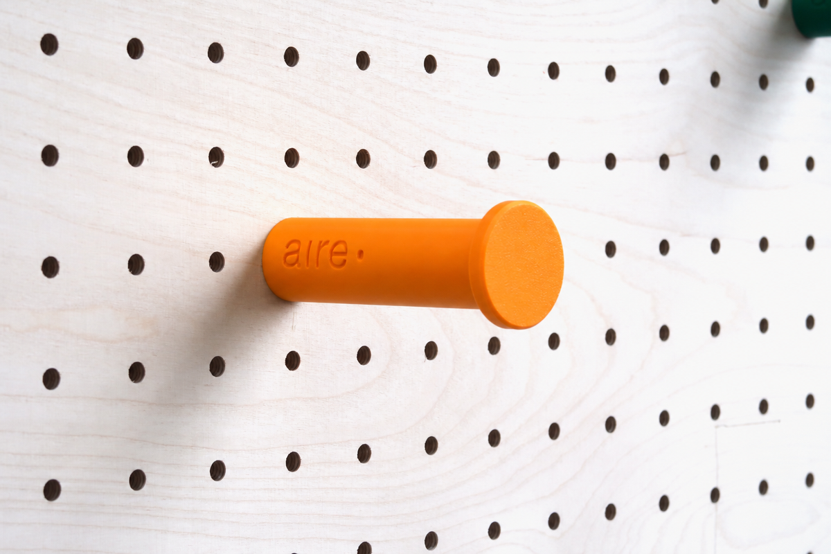 Patère colorée orange fixée sur un pegboard en bouleau