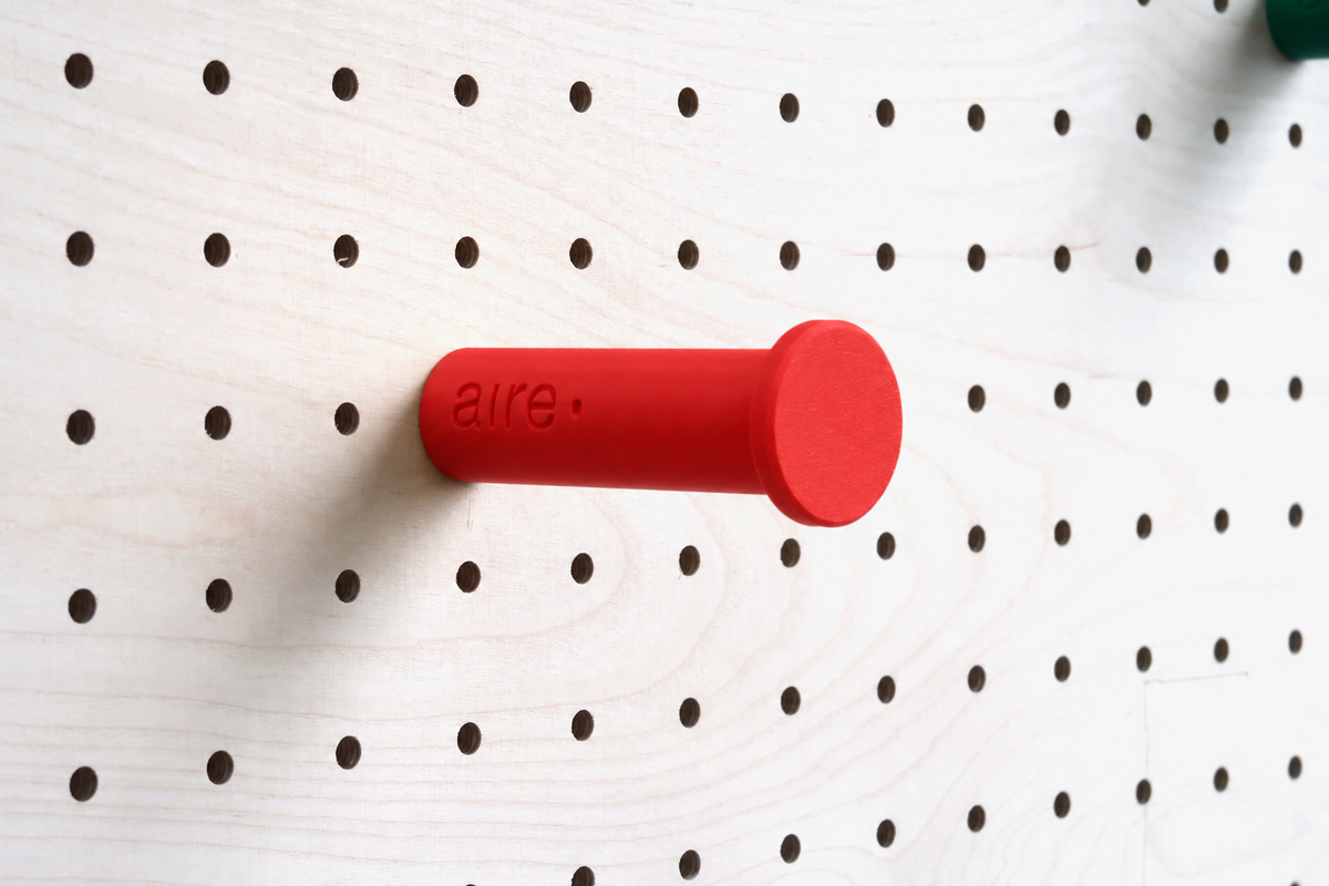 Patère colorée rouge fixée sur un pegboard en bouleau