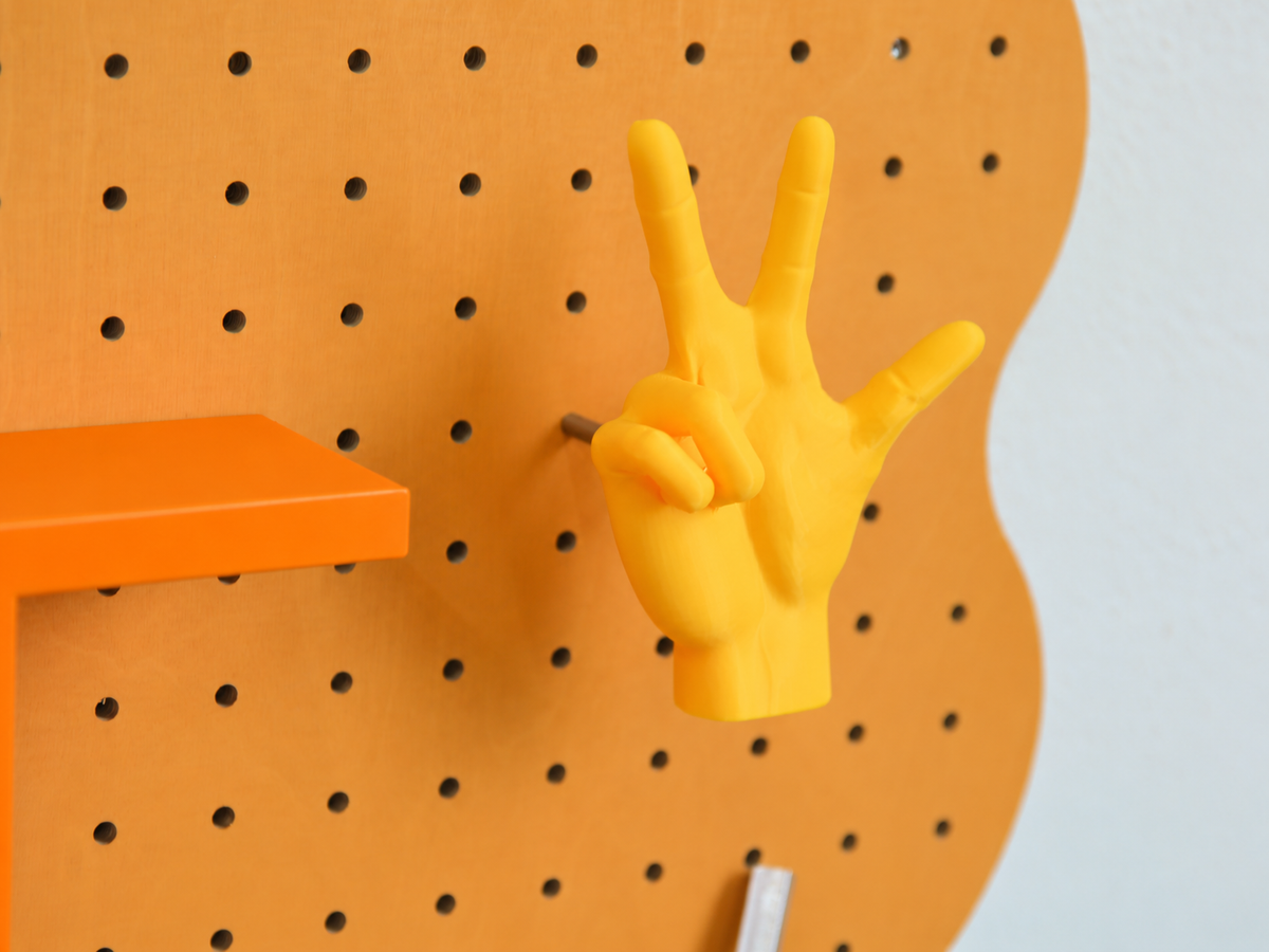 3D-gedruckter Hand-Wandhaken am pastellorangen Pegboard Curves