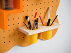 Doppelter hängender Stiftehalter am pastellorangen Pegboard Curves, gefüllt mit Stiften und Filzstiften