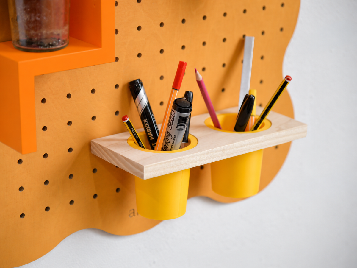 Doppelter hängender Stiftehalter am pastellorangen Pegboard Curves, gefüllt mit Stiften und Filzstiften